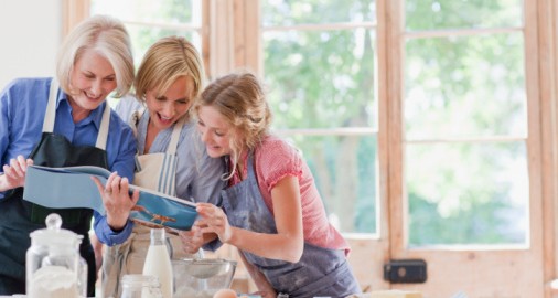 Multi-generation females looking at cookbook and baking in kitchen